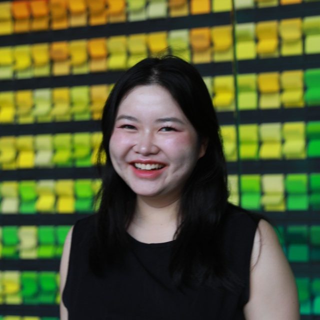 Esther Suebsubanant smiling in front of a wall of yellow and green tiles